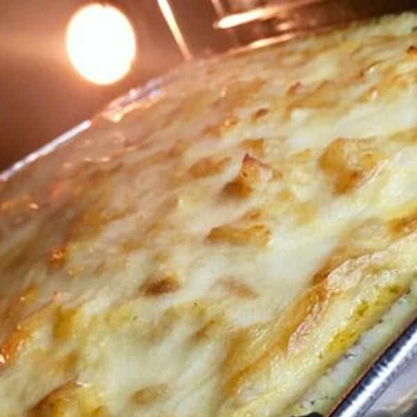A golden-brown Portuguese casserole, possibly bacalhau com natas, baking in an oven with a warm glow.