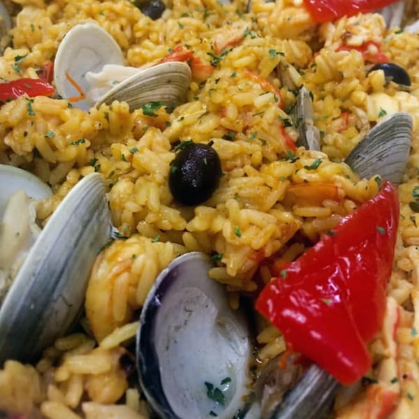 Close-up of Portuguese seafood paella with rice, clams, shrimp, red peppers, and black olives.