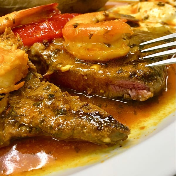 Close-up of a Portuguese steak and shrimp dish with red peppers and a fork, in a rich sauce.