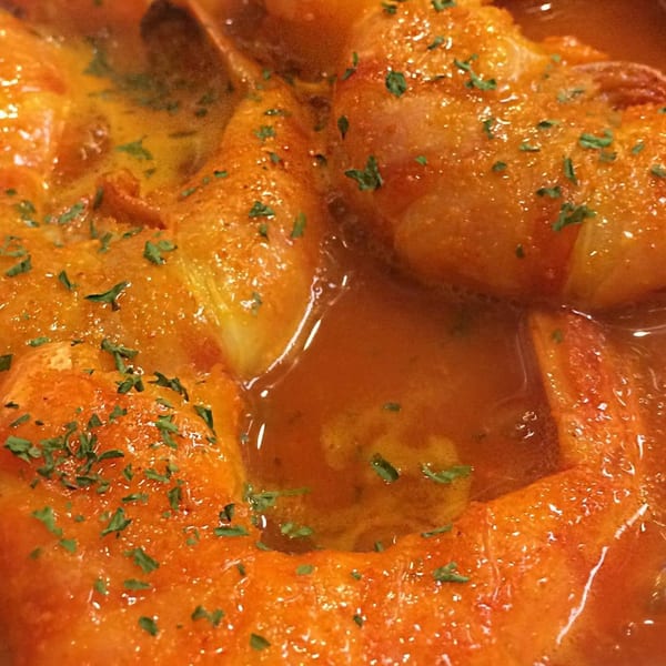 Close-up of Portuguese shrimp in a rich orange sauce, garnished with fresh parsley.